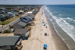 Ein Wohngebiet direkt am Strand mit Häusern, einer Straße und einem Strandabschnitt mit Sonnenschirmen und Menschen.