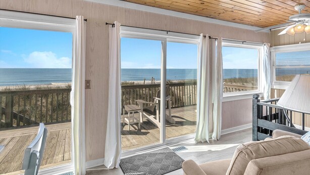 A room with large windows overlooking a beach, a wooden ceiling, and a view of the ocean. - Pelican Crossing: Oceanfront Home w/Spiral Staircase (Oak Island)