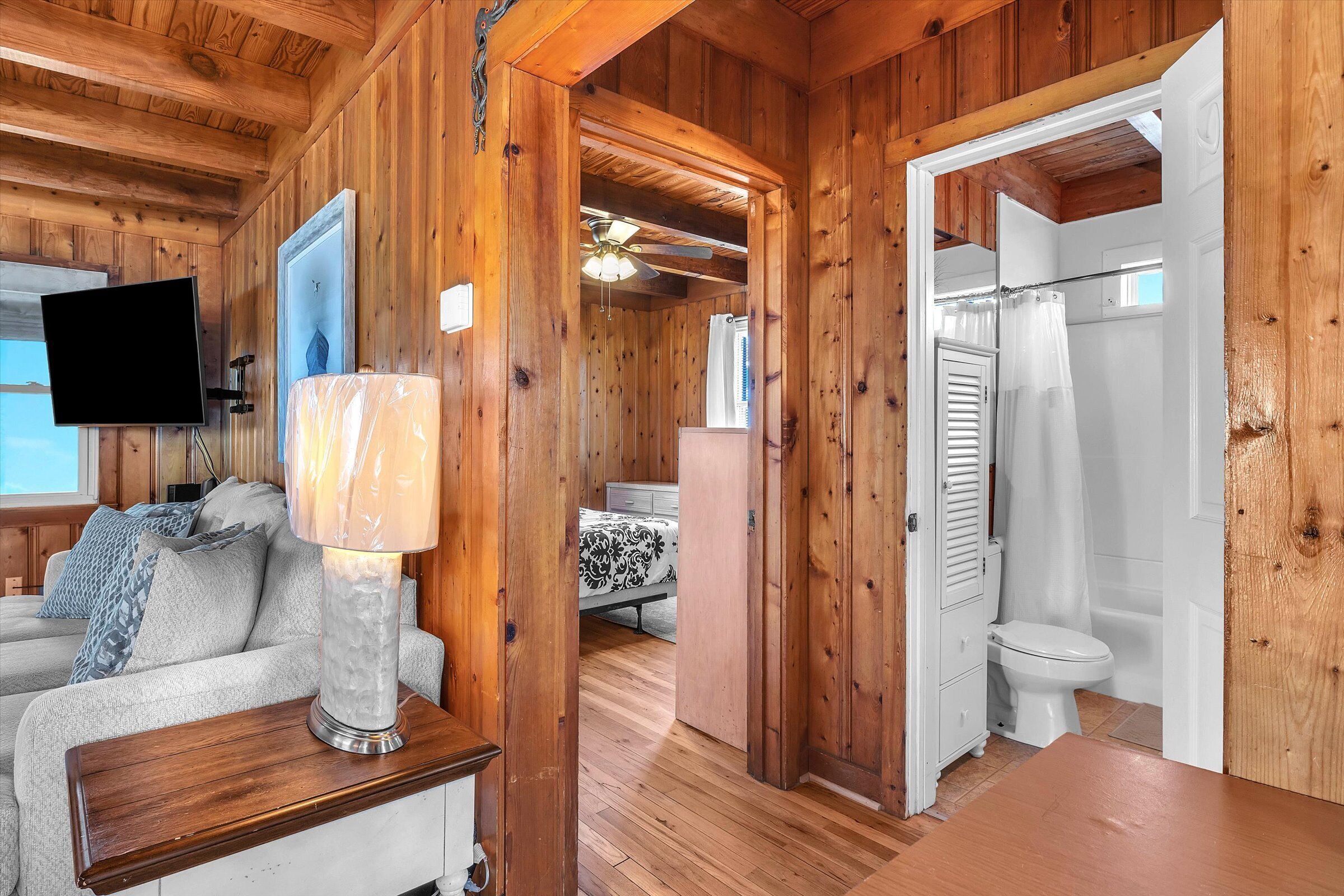 A wooden interior with a sofa, a table with a lamp, a TV, and a bathroom with a shower and toilet.
