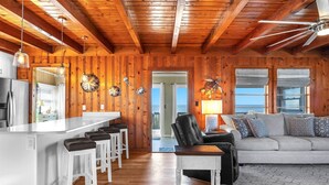 A wooden cabin interior with a kitchen, dining area, and living room. - Pelican Crossing: Oceanfront Home w/Spiral Staircase (Oak Island)