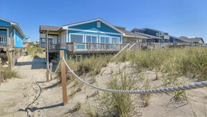 A beachfront property with a wooden deck and a sandy path leading to the entrance. - Pelican Crossing: Oceanfront Home w/Spiral Staircase (Oak Island)