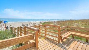 Een houten terras met een bankje met uitzicht op een strand.