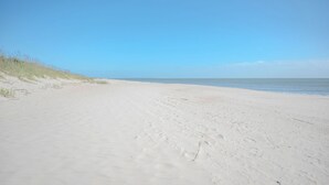 A wide, sandy beach with gentle dunes on the left and a calm sea in the background. - 14 Us: Oceanfront Home with Kayaks, Horseshoe Pit and More Close to Pier (Oak Island)