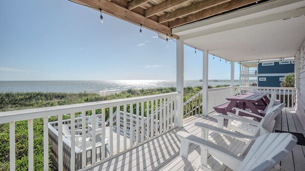 A wooden deck with white railings and a view of the ocean. - 14 Us: Oceanfront Home with Kayaks, Horseshoe Pit and More Close to Pier (Oak Island)