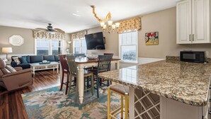 A spacious living area with a sofa, dining table, and chairs, a kitchen with a granite countertop, and a ceiling fan. - 14 Us: Oceanfront Home with Kayaks, Horseshoe Pit and More Close to Pier (Oak Island)