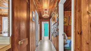 A wooden hallway with a green door at the end, a chandelier, and a bed with a blue and yellow bedspread.