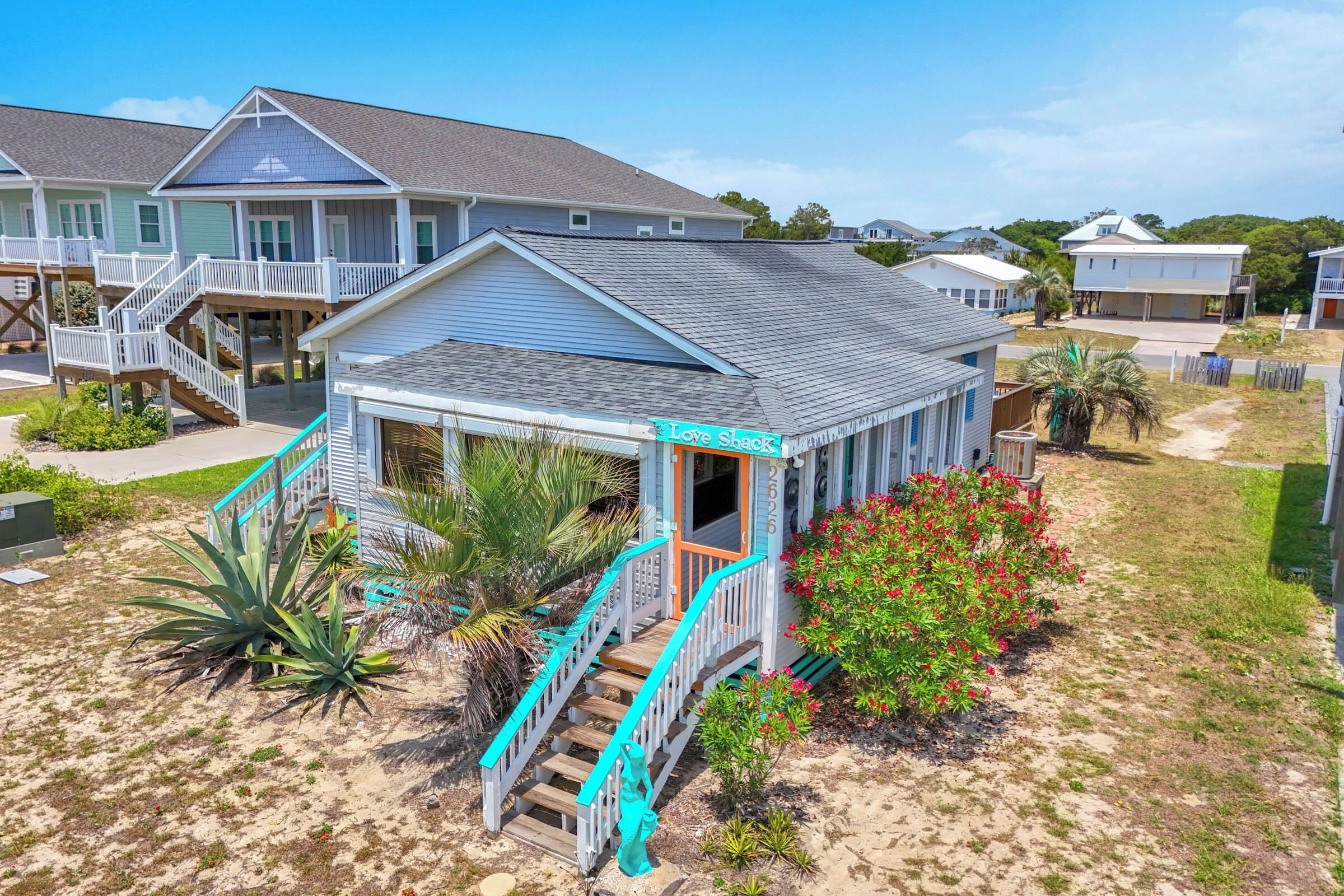 A beachfront property with a covered porch, a staircase leading to a deck, and a sign reading 'Love Shack.'