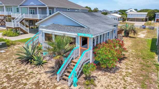 A beachfront property with a covered porch, a staircase leading to a deck, and a sign reading 'Love Shack.'