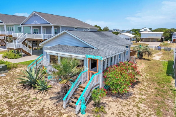 A beachfront property with a covered porch, a staircase leading to a deck, and a sign reading 'Love Shack.'