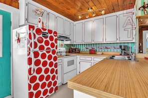 Une cuisine avec des meubles blancs, un réfrigérateur rouge et un plan de travail en bois.