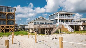 Une propriété située en bord de mer, dotée de structures en bois, notamment d’un bâtiment à plusieurs niveaux avec des balcons et d’un escalier menant à une terrasse en bois.