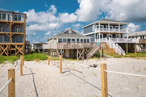 A beachfront property with wooden structures, including a multi-level building with balconies and a staircase leading to a wooden deck.