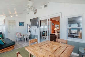 A cozy room with a wooden table, a sofa, and a TV mounted on the wall.
