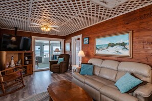 A cozy living room with a wooden ceiling, a leather sofa, a rocking chair, and a television.