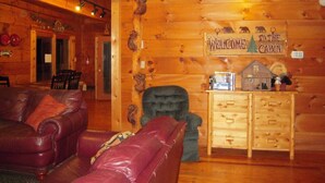 Interior de una cabaña con pared de madera, un sofá de cuero, un mueble de madera y un cartel que dice 'WELCOME TO THE CABIN'.