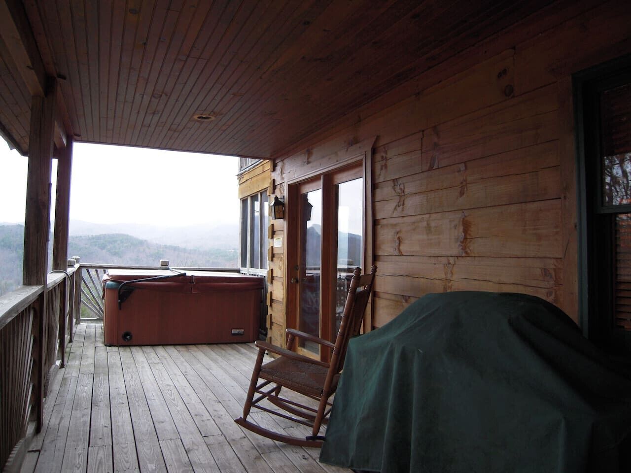 A wooden deck with a hot tub, a rocking chair, and a covered grill.