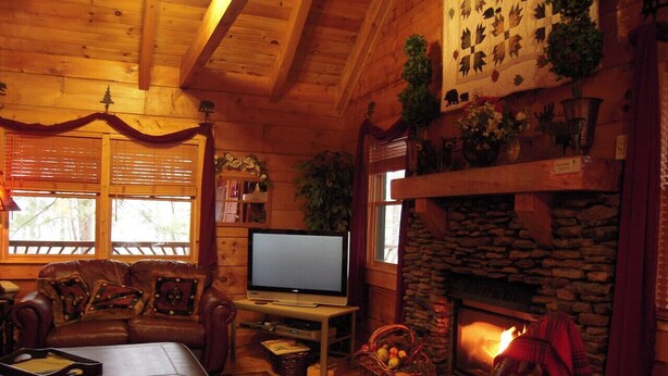 Interior acogedor de una cabaña con chimenea de piedra, mobiliario de madera y una televisión.
