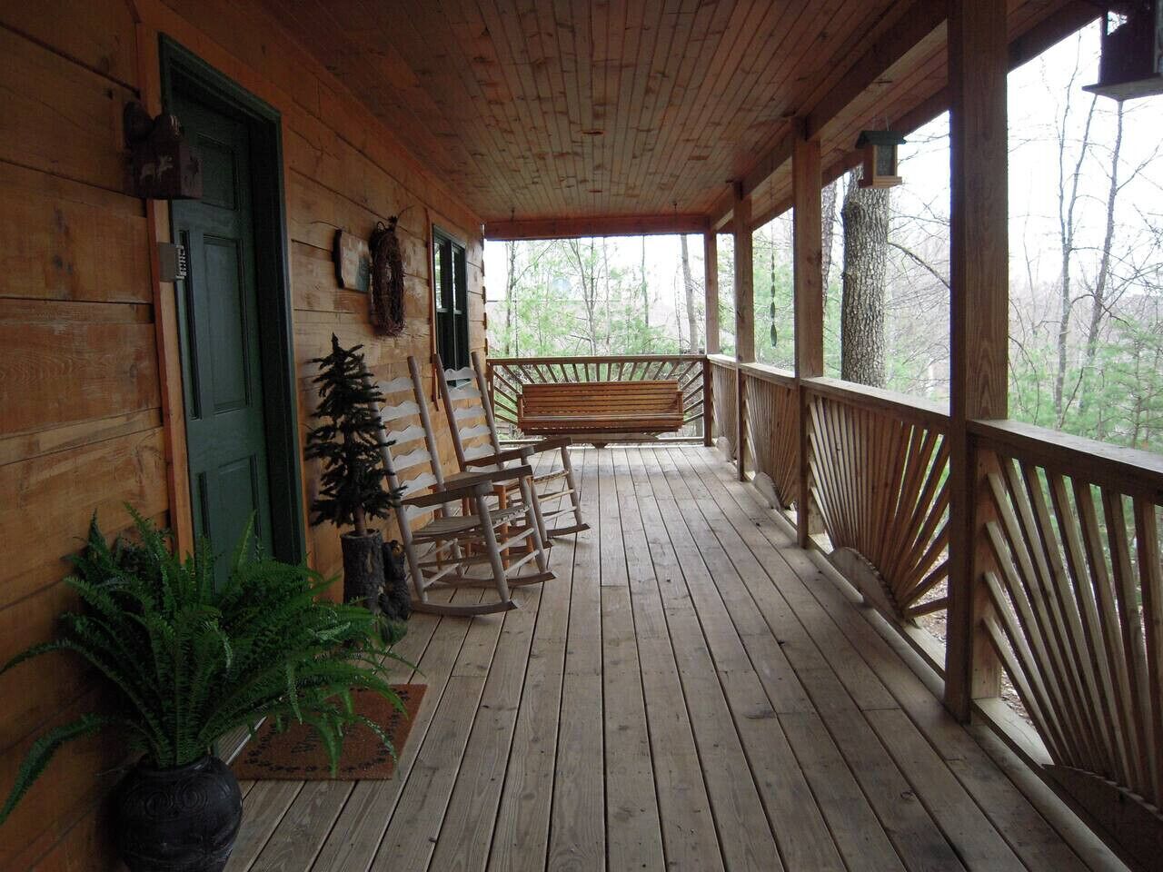 A wooden porch with a bench, potted plants, and a door.