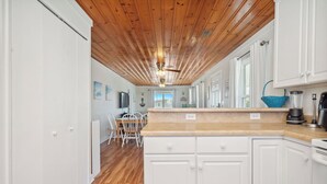 Una cocina con vigas de madera en el techo, armarios blancos y encimera de madera.