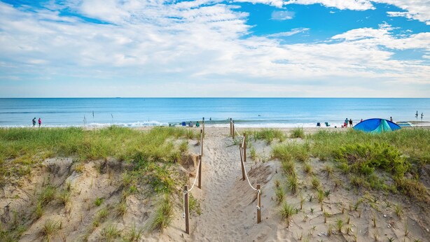 A sandy beach path leading to the ocean with a tent and people in the distance. - A Pirate's Paradise: Oceanfront Home with Covered Porch and Porch Swing (Oak Island)