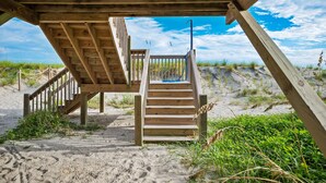 A wooden staircase leading to a beach area with a clear sky and sand dunes in the background. - A Pirate's Paradise: Oceanfront Home with Covered Porch and Porch Swing (Oak Island)