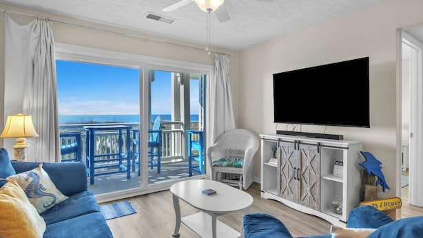 Un salon comprenant un canapé, une table basse, un téléviseur et un balcon avec vue sur l’océan.
