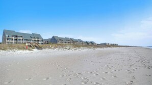 Un hôtel situé en bord de mer, composé de plusieurs bâtiments, avec une plage de sable et des empreintes de pas bien visibles.