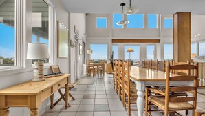 Un comedor espacioso con una larga mesa de madera y sillas, ventanas amplias y vistas al mar.