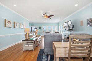 Un salon avec un ventilateur de plafond, un téléviseur fixé au mur, un canapé, une table basse et une table à manger.
