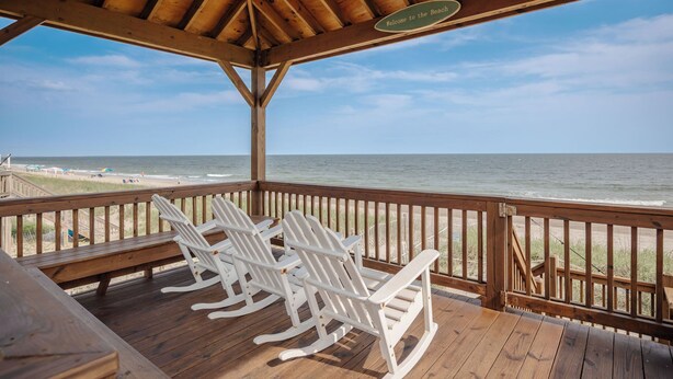 A wooden deck with rocking chairs overlooking the beach.