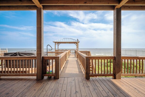 Une terrasse en bois menant à une plage, avec un espace abrité et une vue sur l’océan.