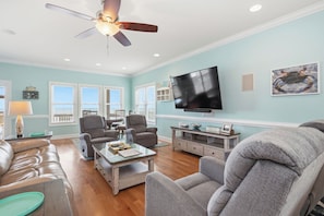 A spacious living room with a ceiling fan, a flat-screen TV, and a dining area with a table and chairs.