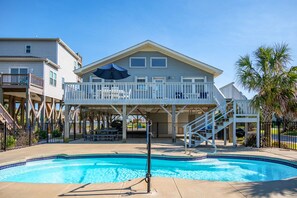A pool area with a covered deck, stairs leading to a second floor, and a clear blue pool.