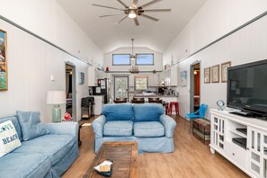A spacious living room with a blue sofa, a wooden coffee table, and a TV on a white cabinet.
