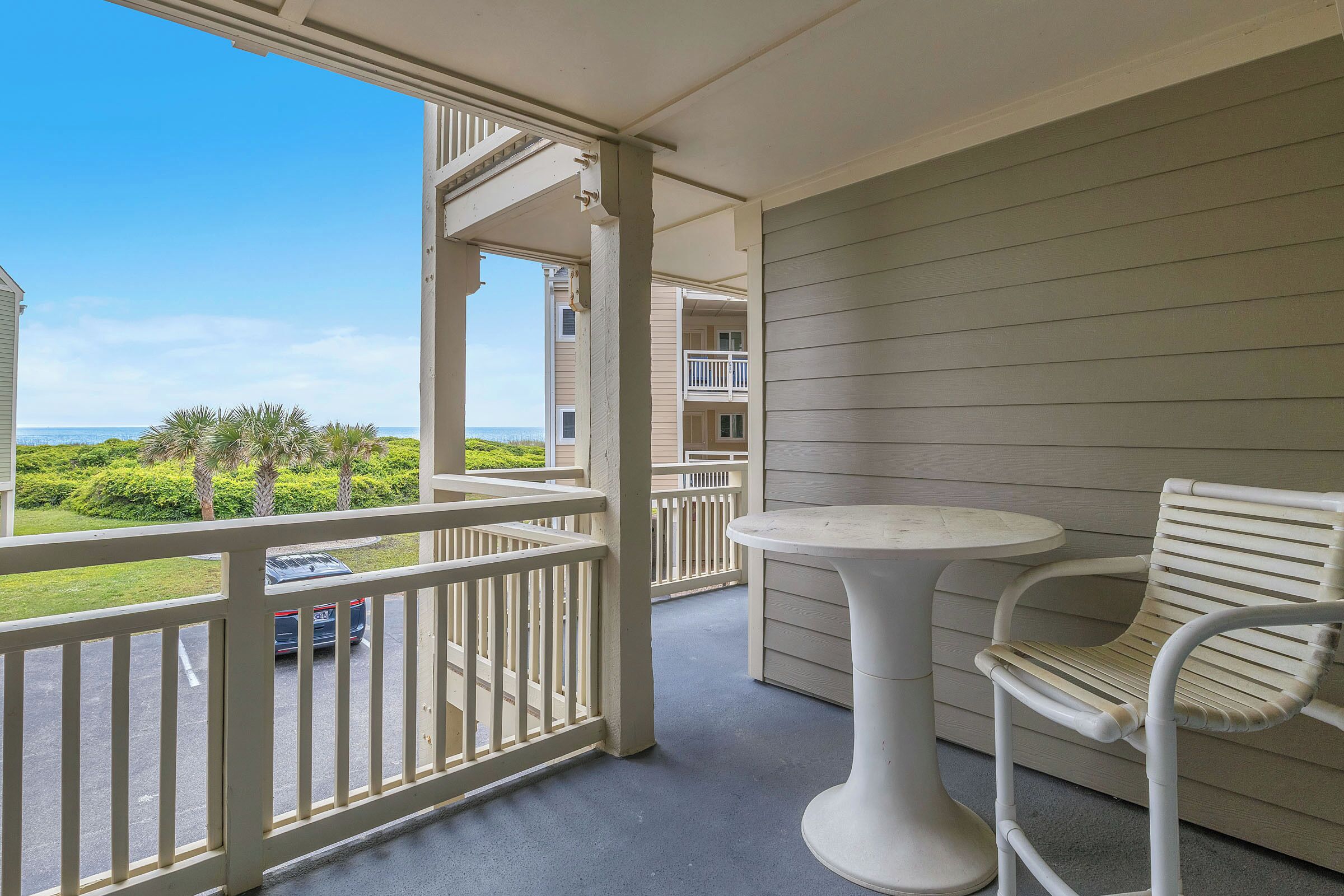 A balcony with a white railing, a round table, and a wicker chair.