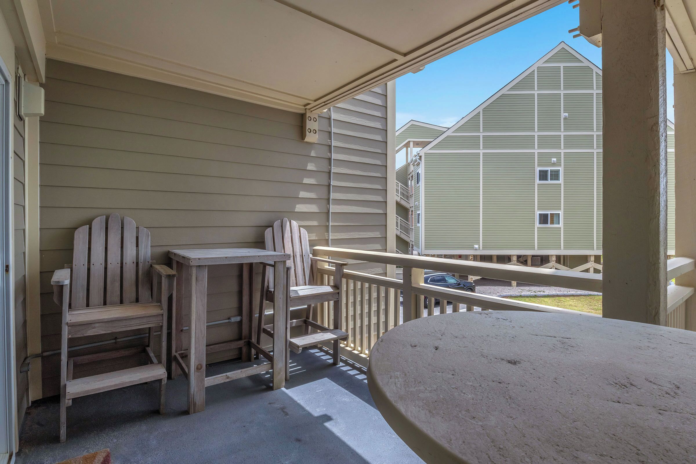 A balcony with a wooden chair and table, a railing, and a view of neighboring buildings.