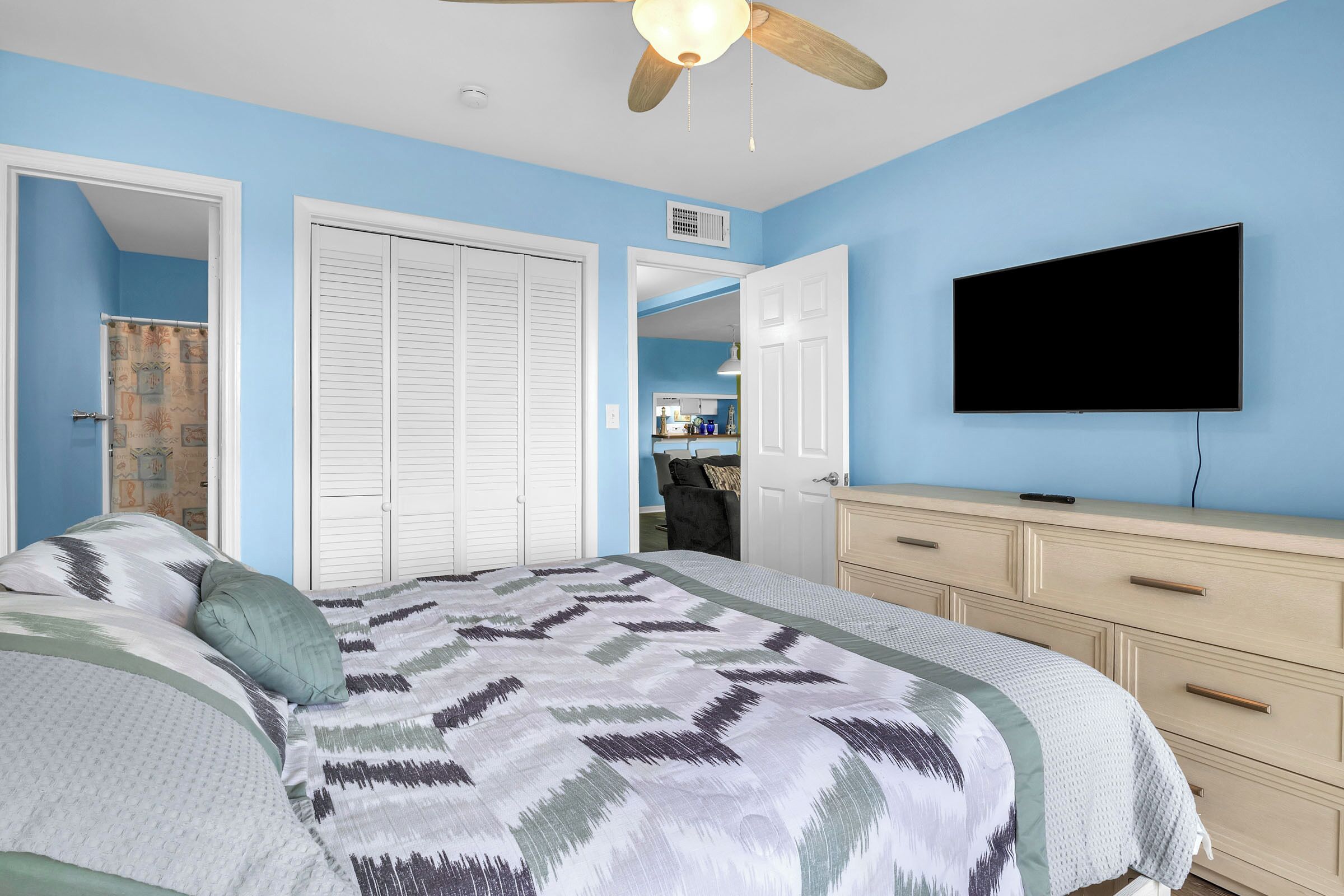 Een slaapkamer met een bed, een plafondventilator, een televisie en een dressoir.