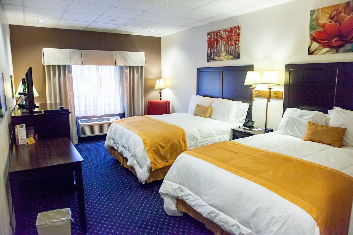 A hotel room with two beds, a desk, a chair, a TV, and a painting on the wall.