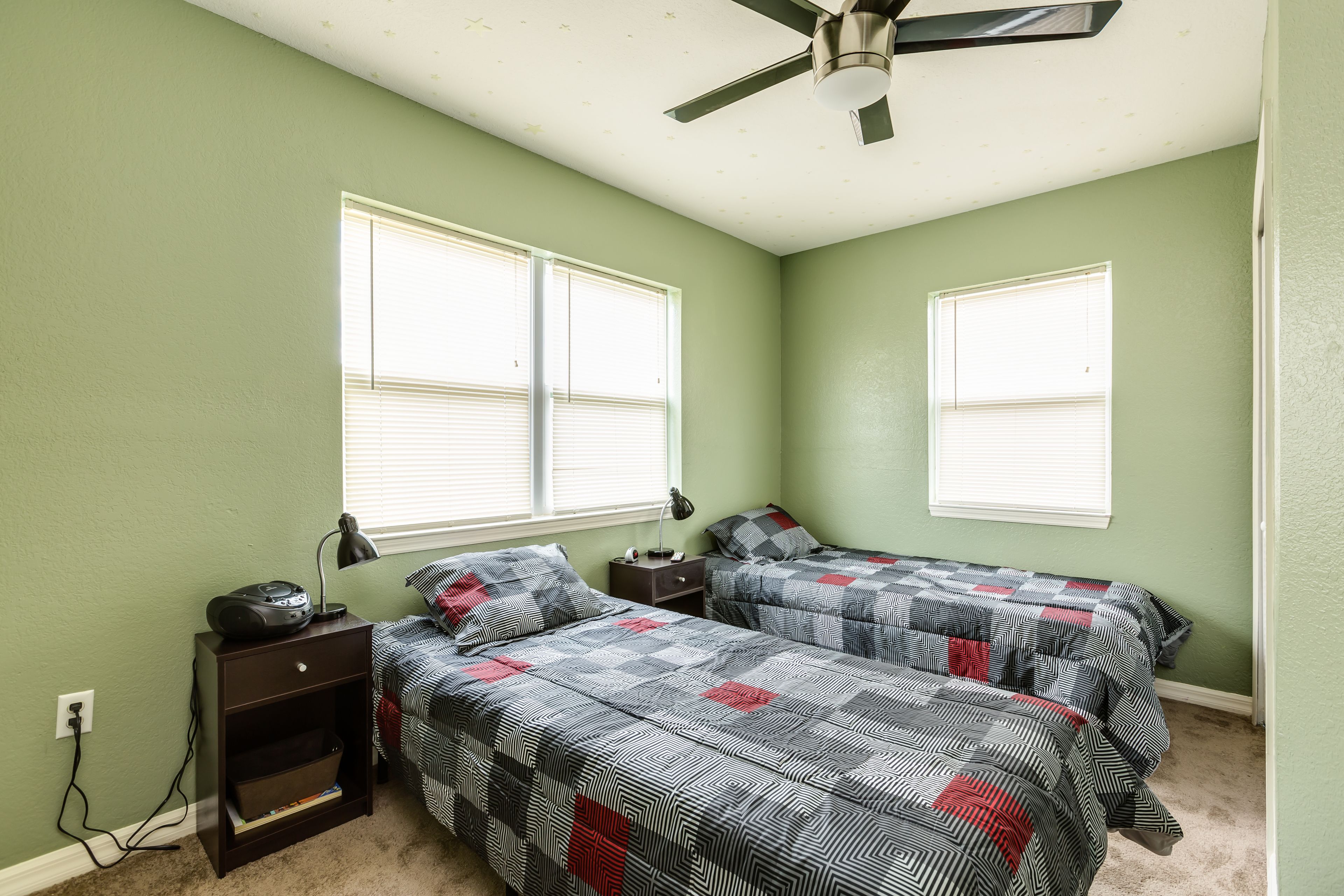 A bedroom with two beds, a nightstand with a lamp, and a ceiling fan.