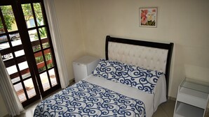 A bedroom with a bed, a nightstand, a window with a view of the street, and a wall-mounted picture. - Pousada Cores do Mar (Paraty)