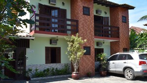 A two-story building with a balcony, potted plants, and a parked car. - Pousada Cores do Mar (Paraty)