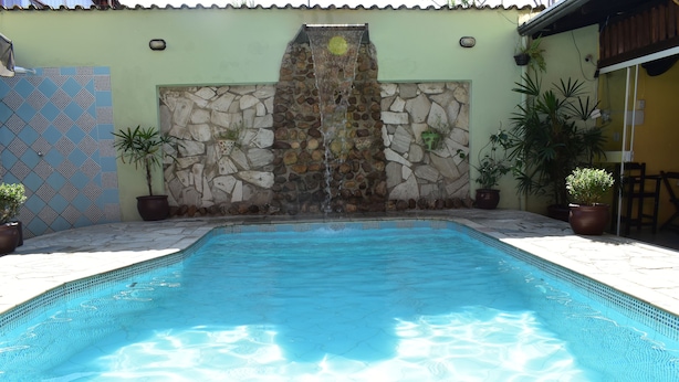 A swimming pool with a stone waterfall feature, surrounded by potted plants and a patterned wall. - Pousada Cores do Mar (Paraty)