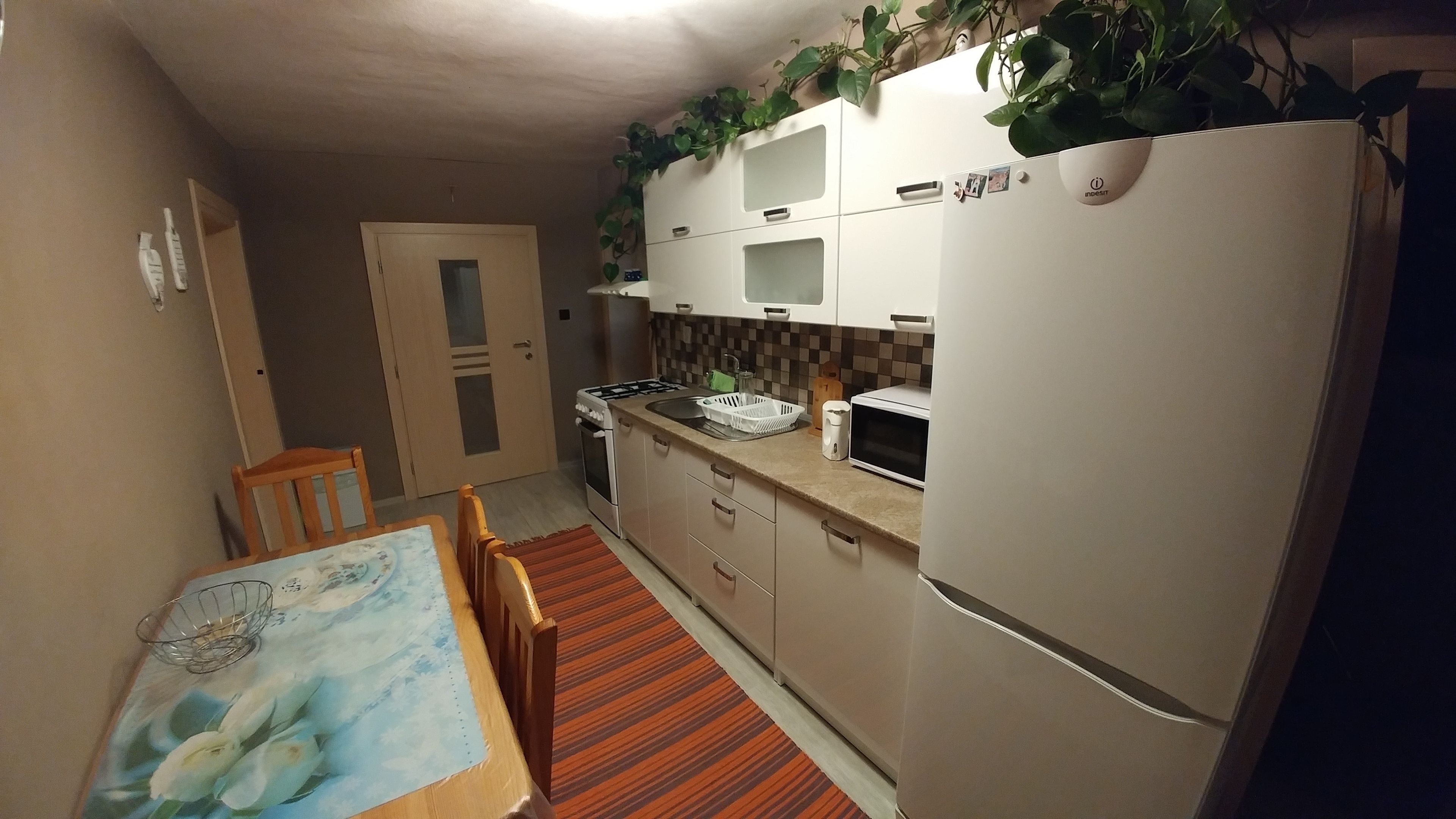 Eine kompakte Küche mit Kühlschrank, Mikrowelle und Herd. Ein Esstisch mit Stühlen und einem gemusterten Tischläufer.