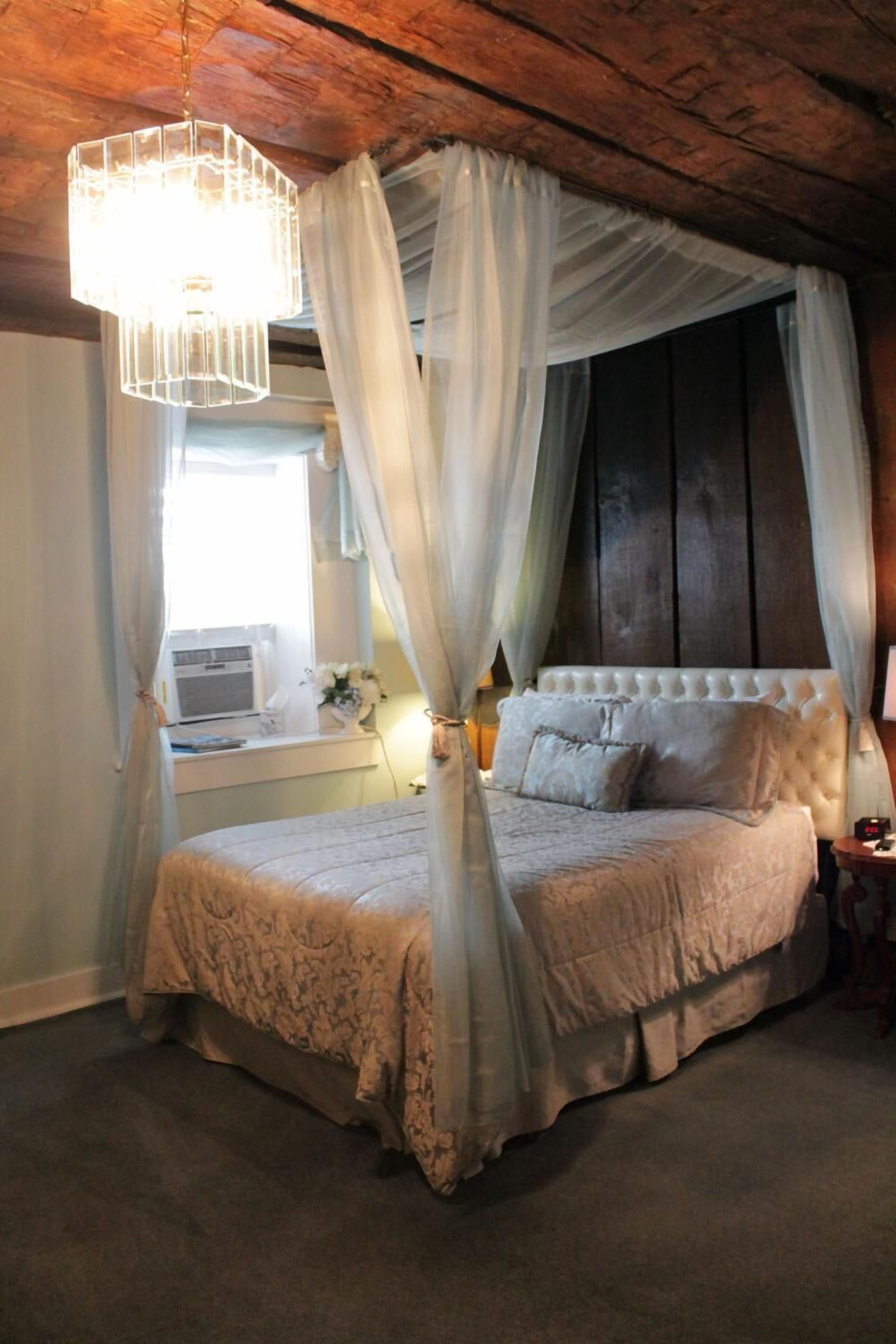 A bedroom with a canopy bed, a bedside table, and a window with curtains.