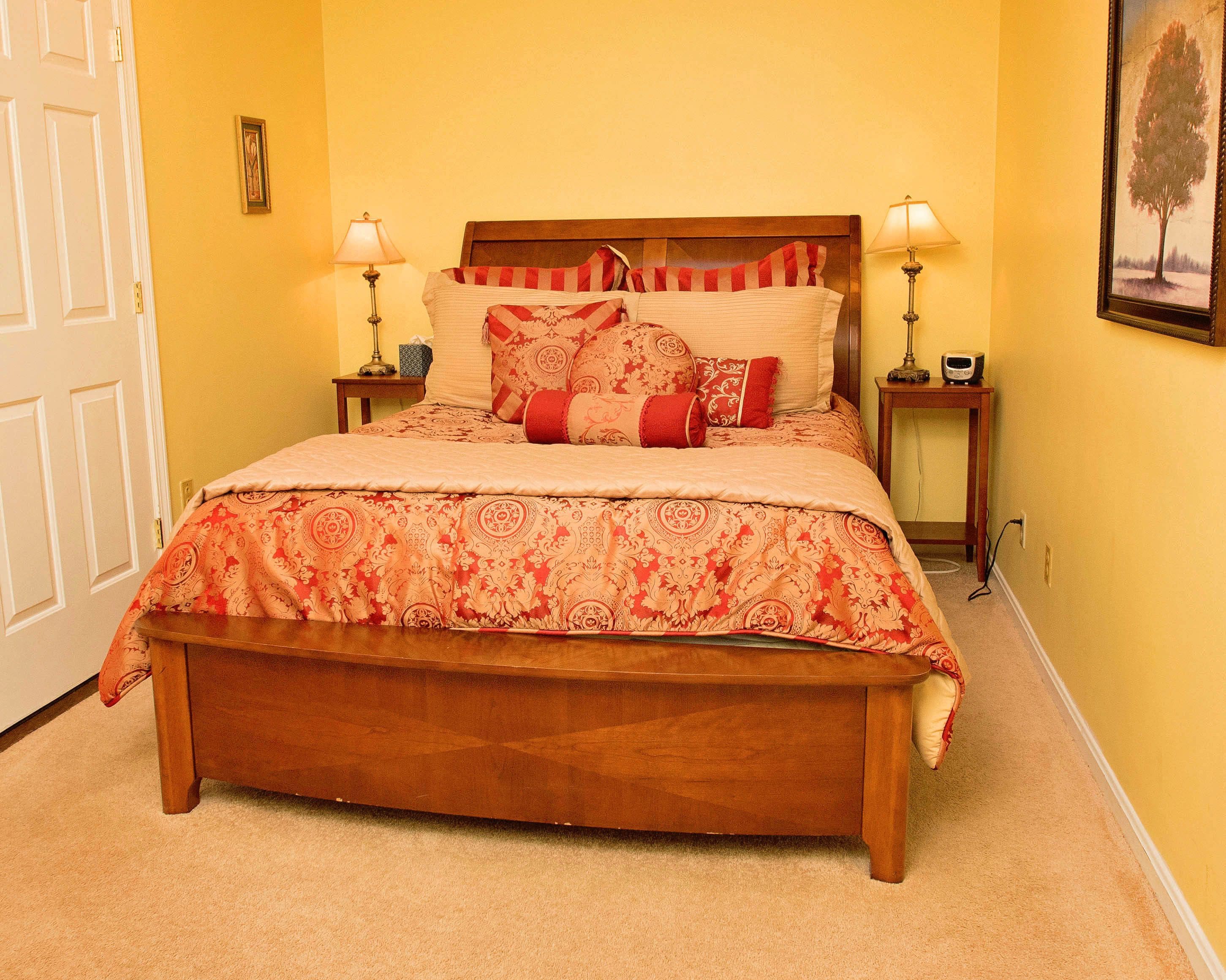 A bedroom with a wooden bed, patterned bedding, two bedside tables with lamps, and a framed picture on the wall.