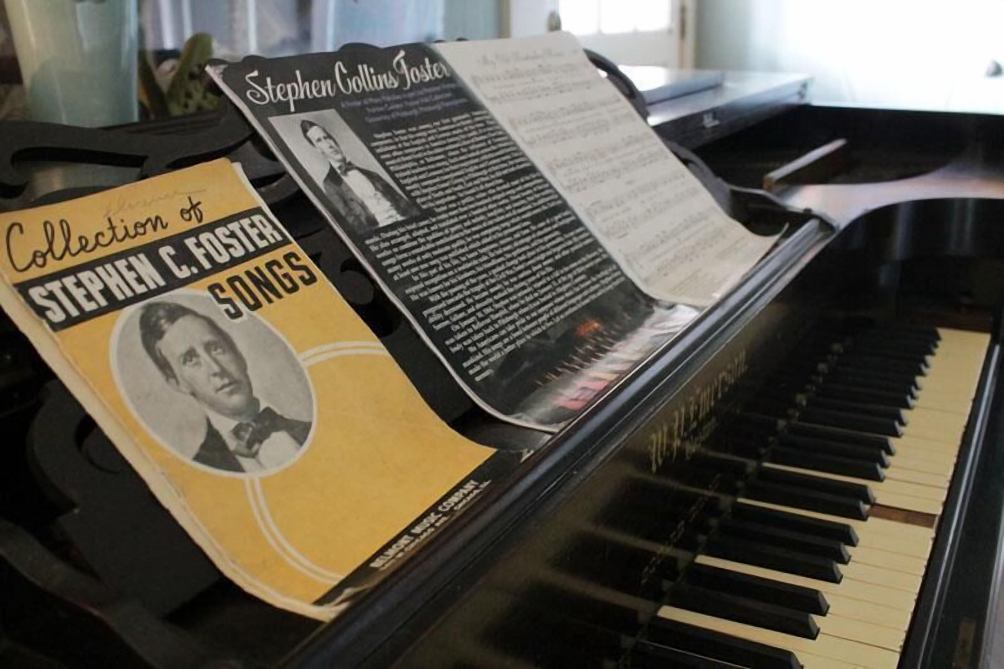 A piano with sheet music titled "Collection of Stephen C. Foster Songs" and a biography of Stephen Collins Foster.