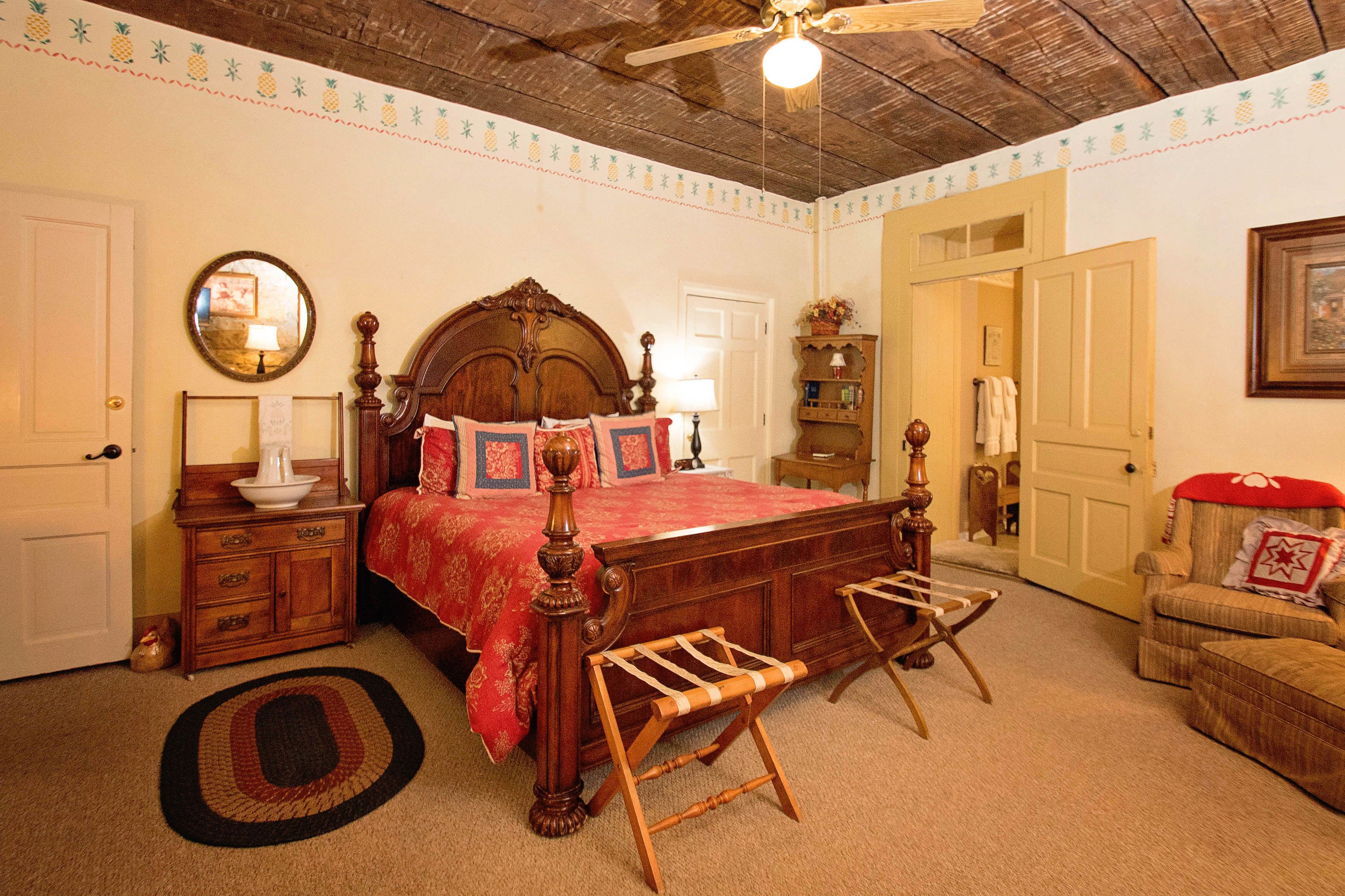A bedroom with a wooden bed, a wooden bench, a mirror, a lamp, and a door.