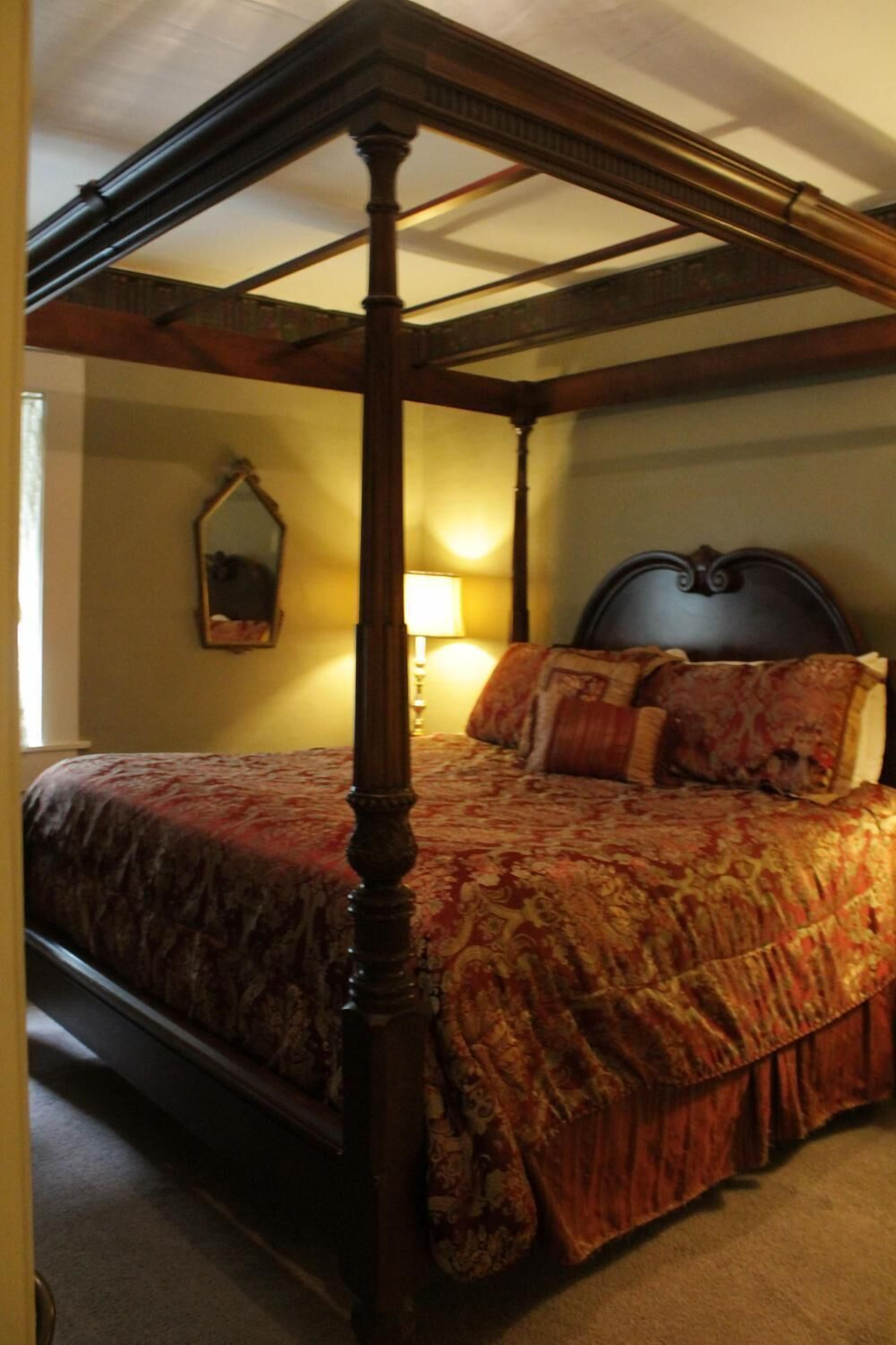 Una cama con dosel, cabecera oscura y colcha con motivos florales.