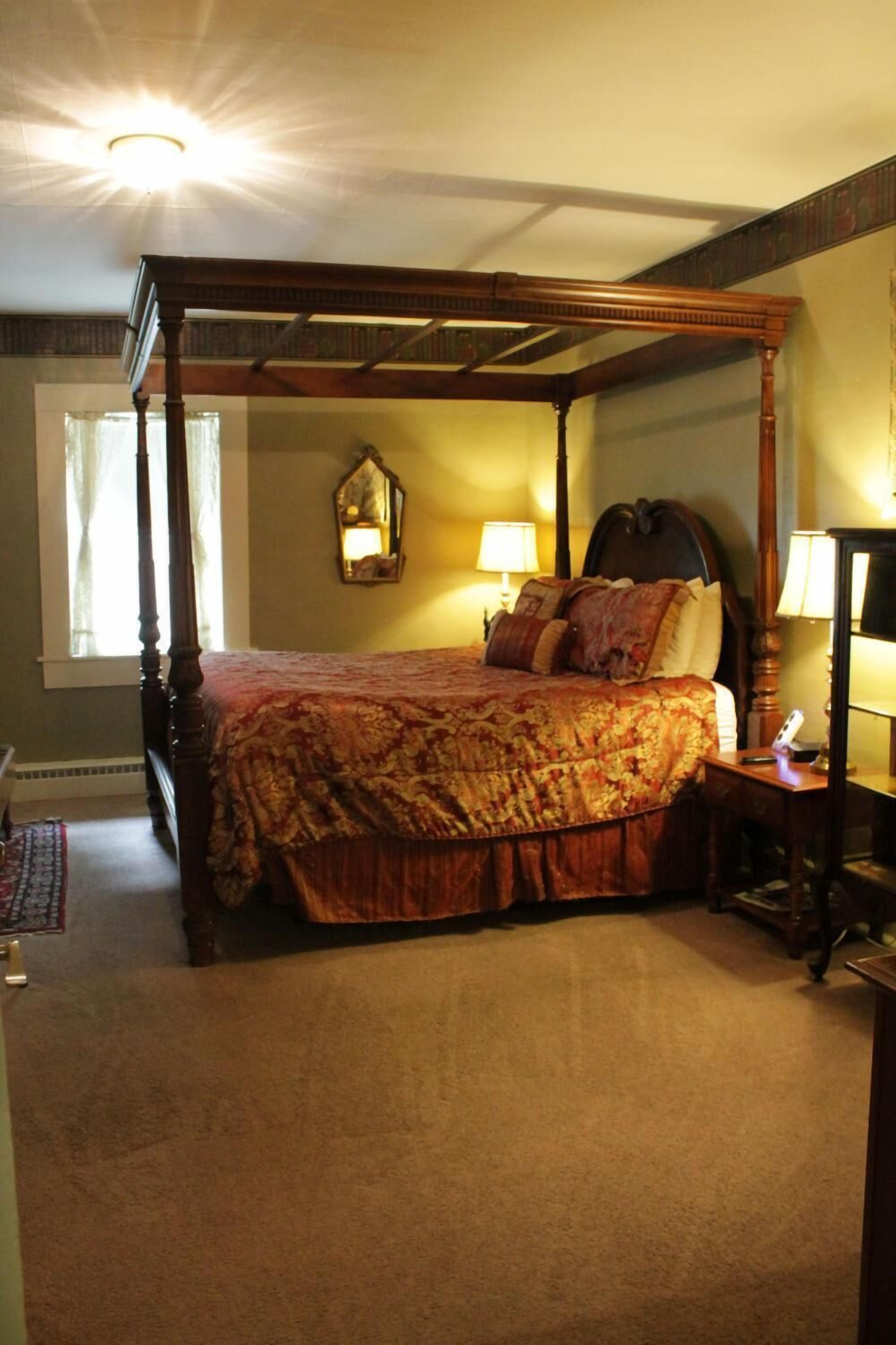 A four-poster bed with a floral bedspread, a nightstand with a lamp, and a wall-mounted mirror.