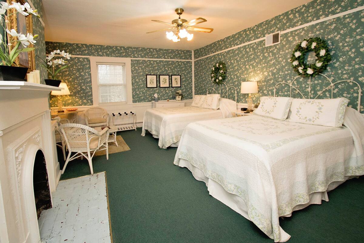 A bedroom with two beds, a fireplace, a chandelier, and floral wallpaper.